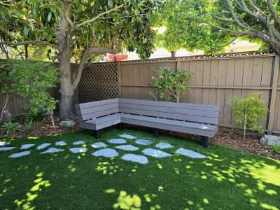 Turf lawn with concrete stepping pads leading to a built-in bench along the fence