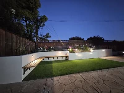 Backyard at dusk with a lit built-in seat wall beside an artificial turf lawn