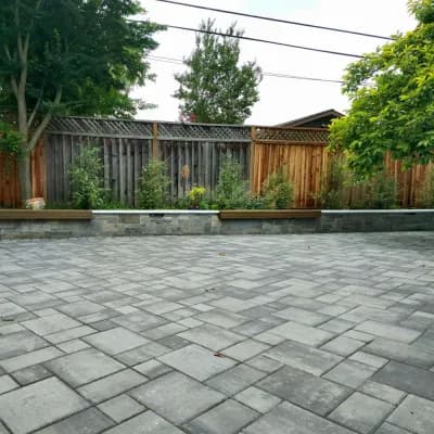 Grey paver patio bordered by a raised planter bed and a wood fence