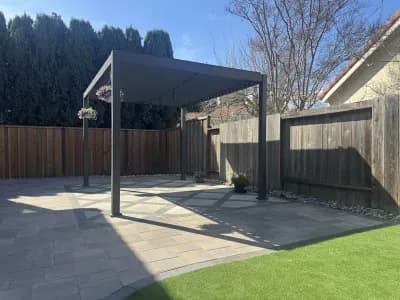 Modern dark-framed pergola over a paver patio beside an artificial turf lawn
