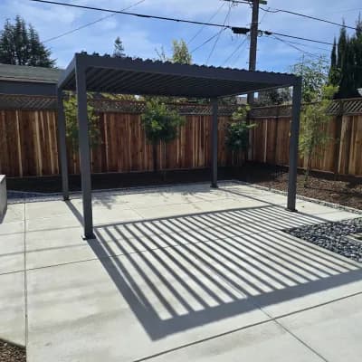 Dark louvered pergola casting striped shadows across a paver patio