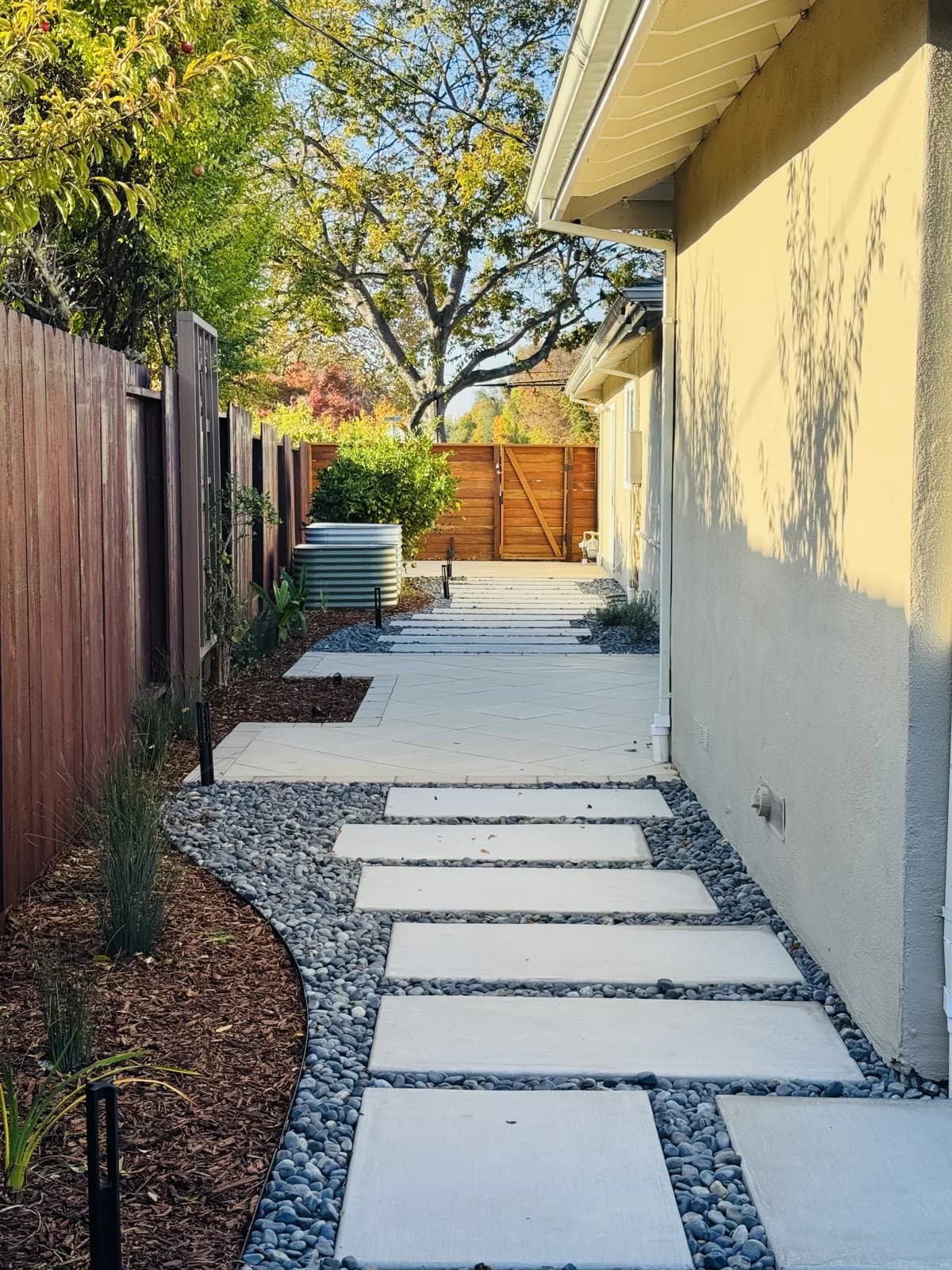 Side yard path of concrete steppers in river rock with new plantings and path lights