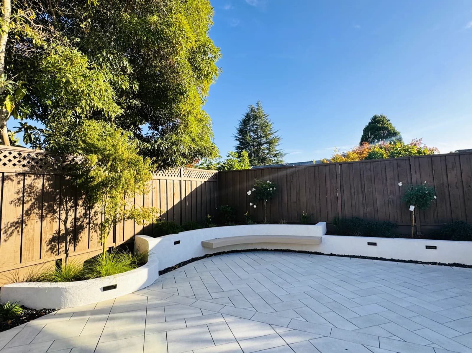 Curved white seat wall with planters along a large-format paver patio