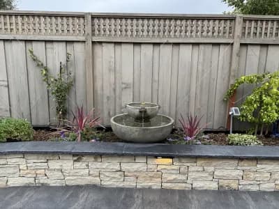 Stone retaining wall with a tiered fountain and planting along the top