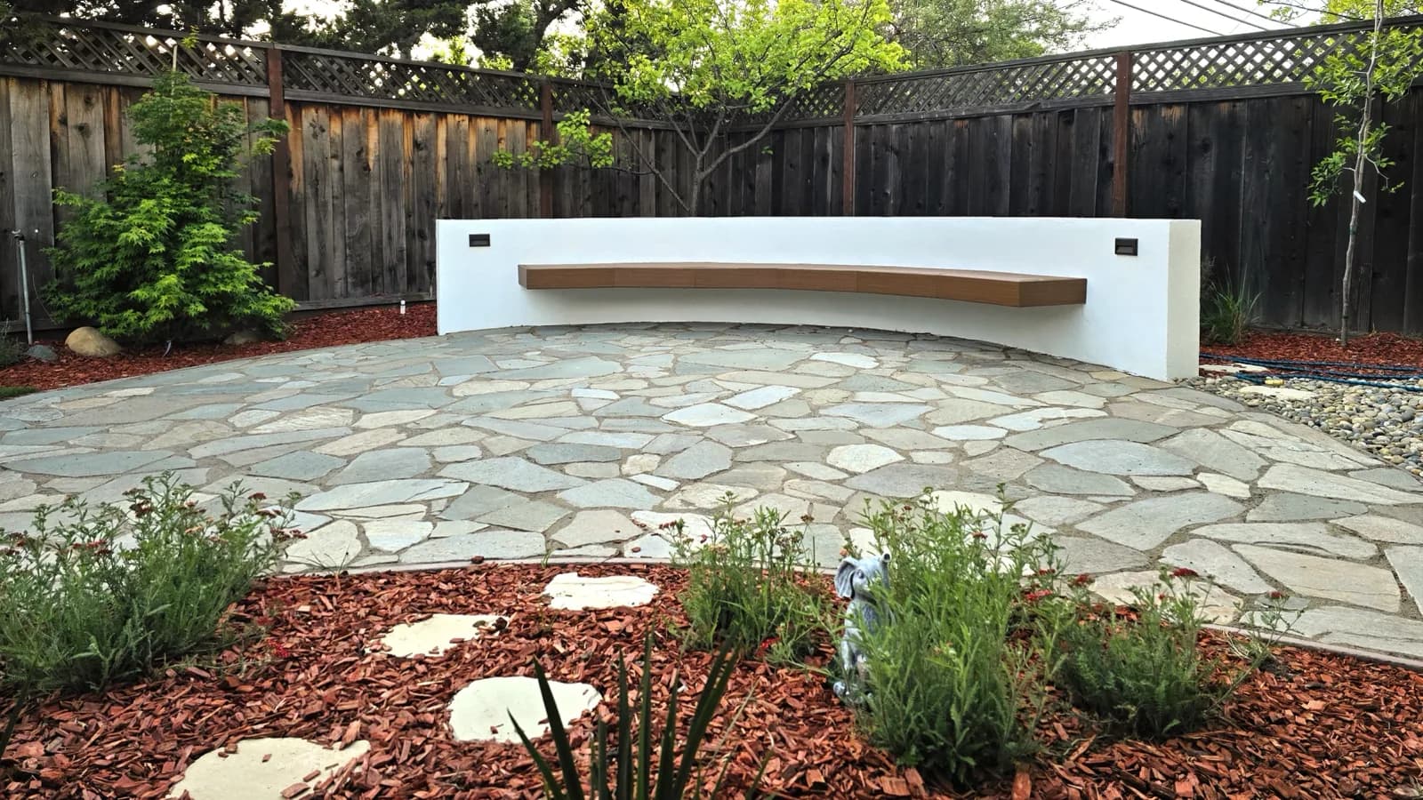 Flagstone patio with a floating wood bench on a white seat wall and bark mulch planting beds