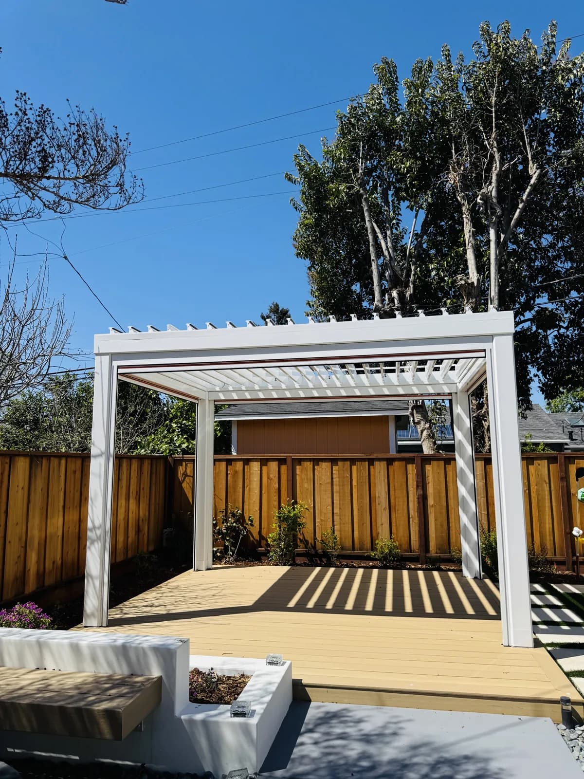 White louvered pergola over a composite deck with a built-in white planter