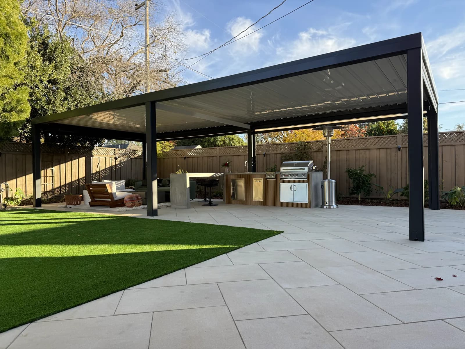 Large black louvered pergola over an outdoor kitchen with a built-in grill on a paver patio