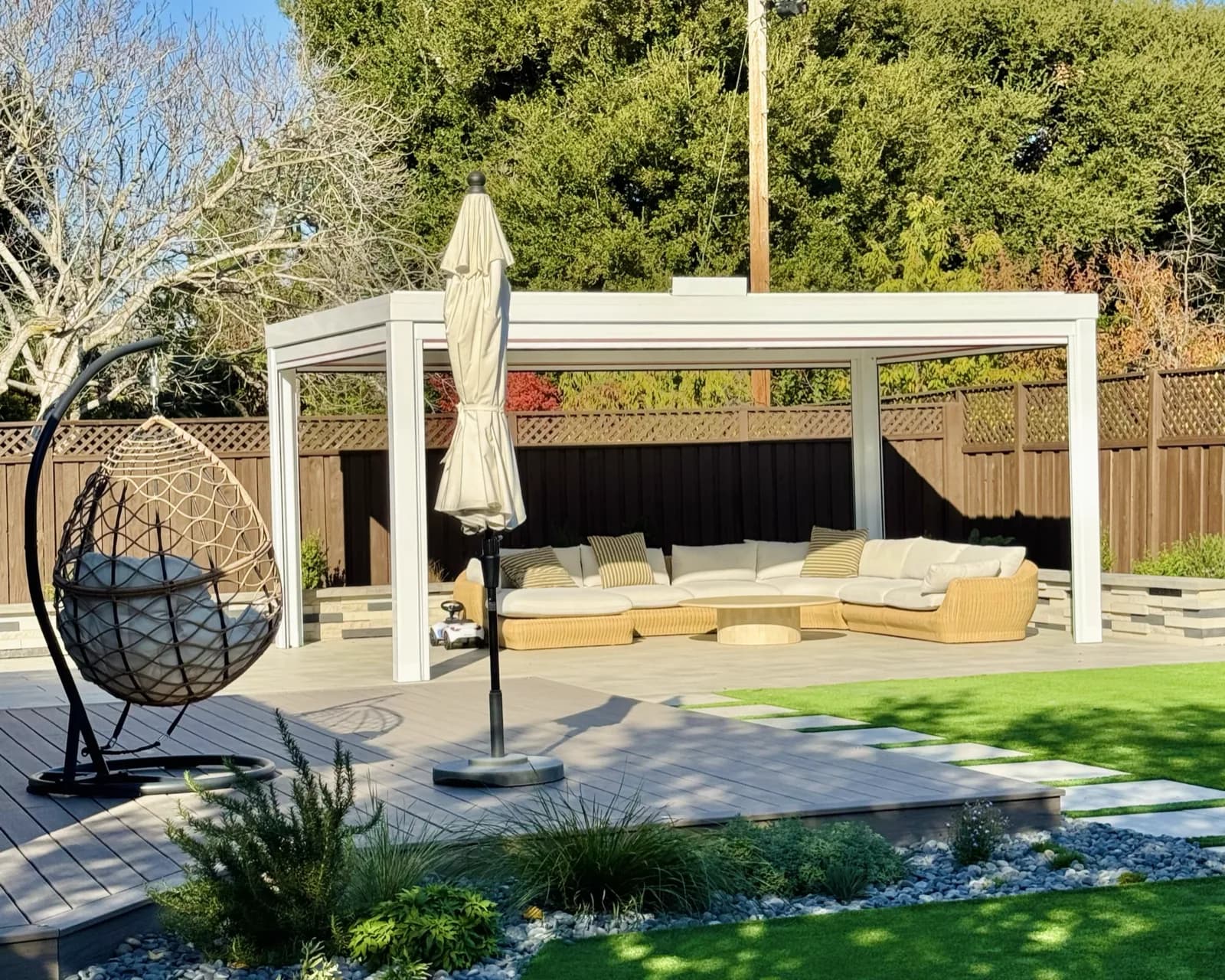 White pergola with lounge seating and a hanging egg chair on a composite deck