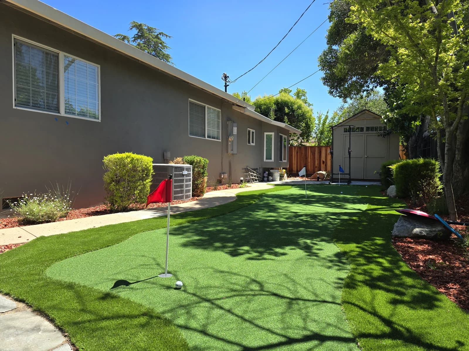 Artificial turf backyard with a putting green beside a garden shed
