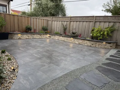 Curved concrete patio with a lit low retaining wall and gravel border
